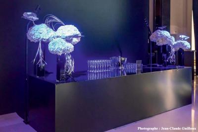 Une voiture de luxe bleue exposée dans un showroom, un homme examine l'intérieur par la portière ouverte.