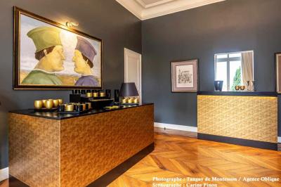 Salle lumineuse avec parquet en bois, table ronde dressée avec nappe rouge, et moulures décoratives au plafond.