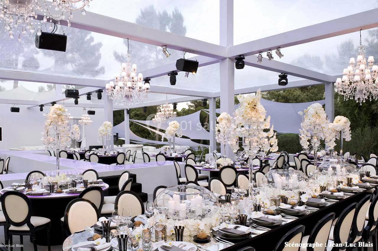 Salle de réception élégante avec tables décorées de fleurs blanches, chandeliers et verrière laissant passer la lumière…