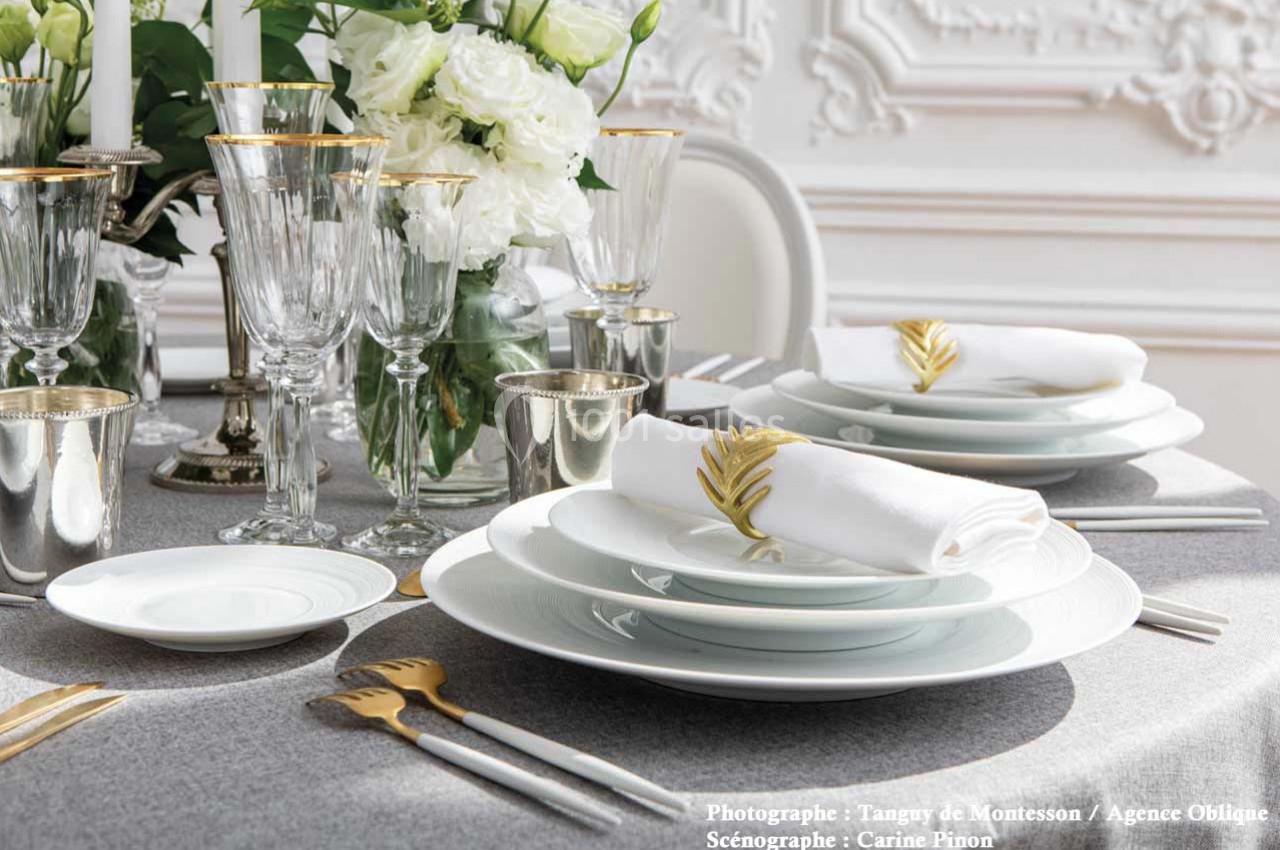 Table élégamment dressée avec vaisselle blanche, couverts dorés, verres en cristal et décor floral blanc.