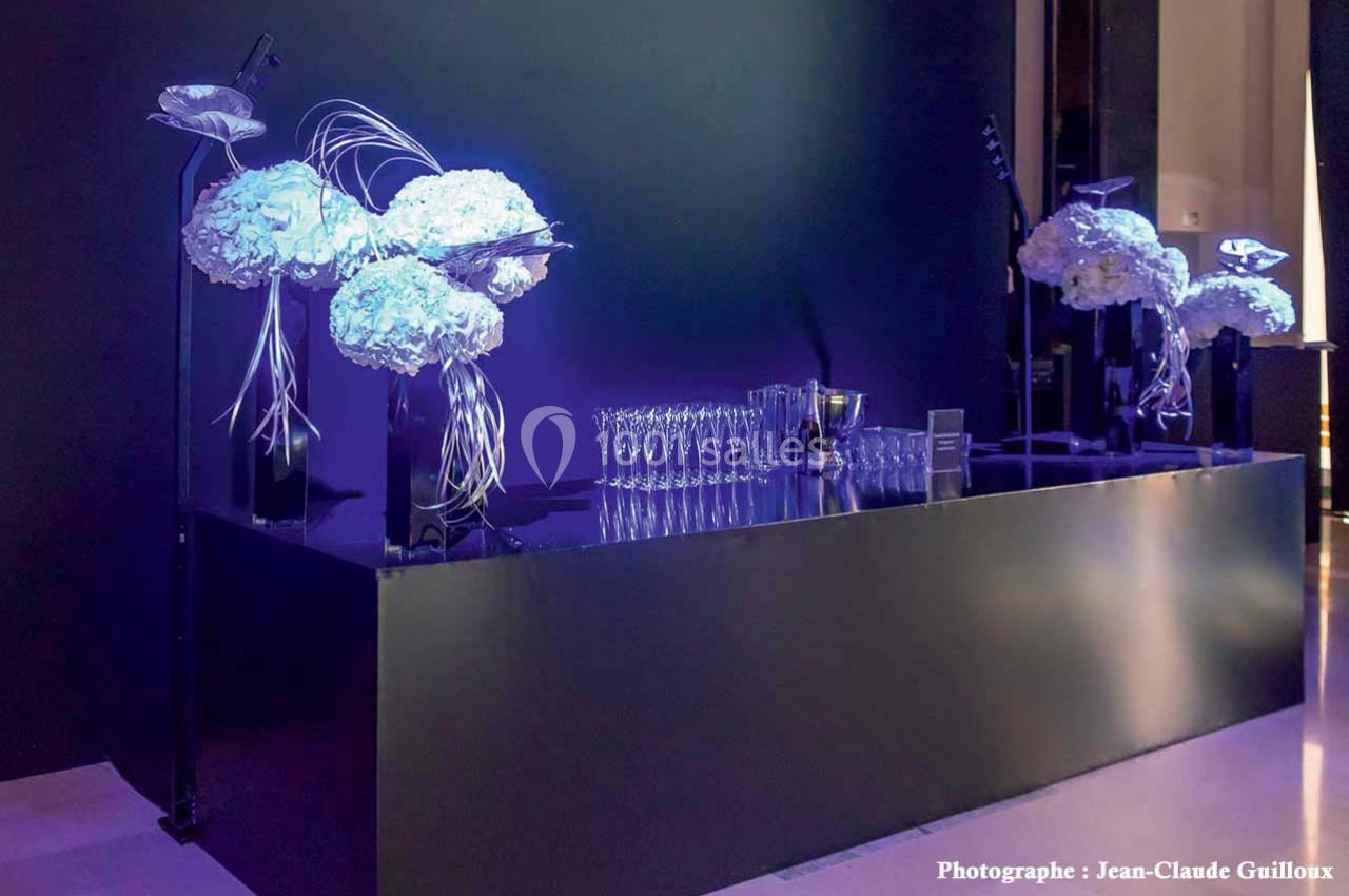 Table noire élégante décorée de fleurs blanches et de verres alignés, éclairée par une lumière violette.