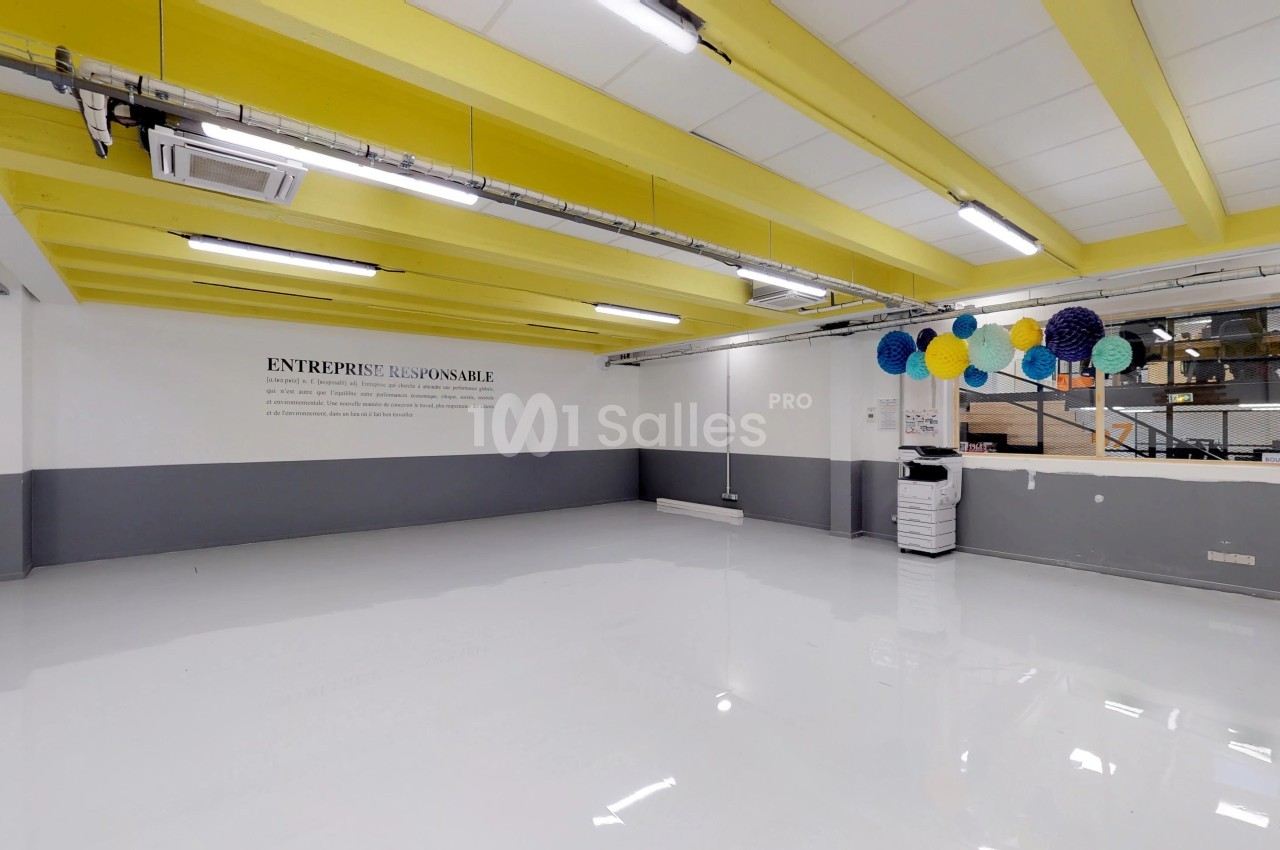 Salle vide avec sol brillant, murs gris et blancs, plafond jaune, décorations suspendues et texte mural visible.