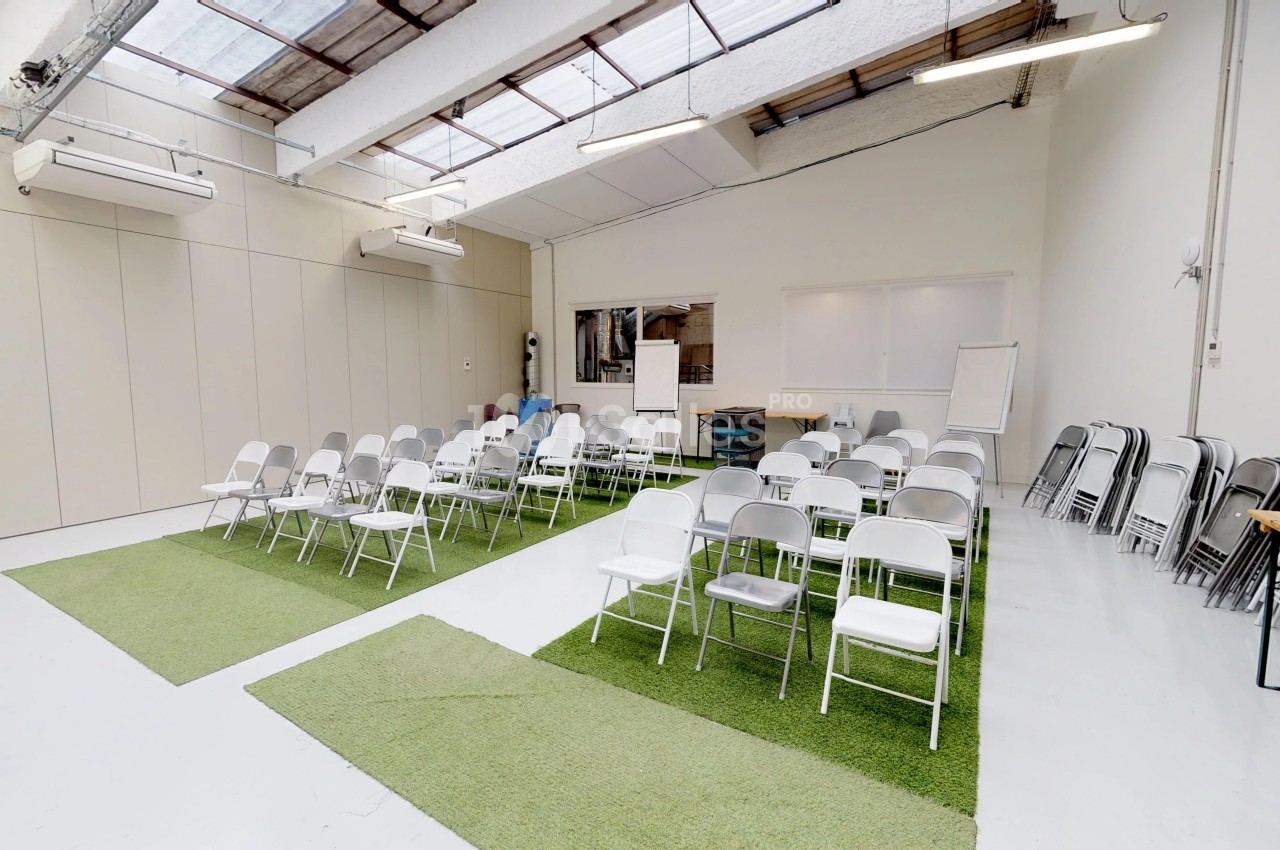 Salle lumineuse aménagée avec des chaises blanches disposées en rangées sur des tapis verts, prête pour une réunion.