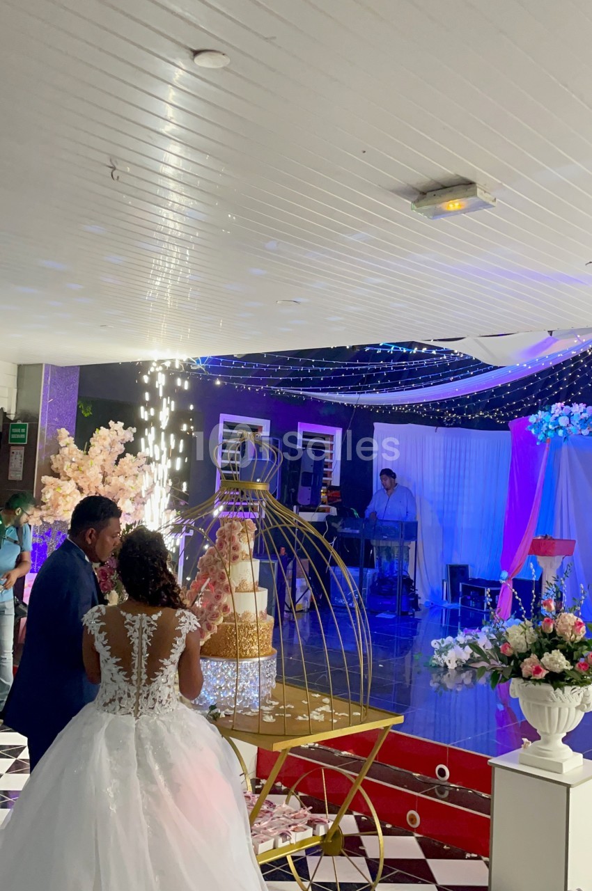 Un couple en tenue de mariage coupe un gâteau décoré, entouré de fleurs et d'une ambiance lumineuse festive.
