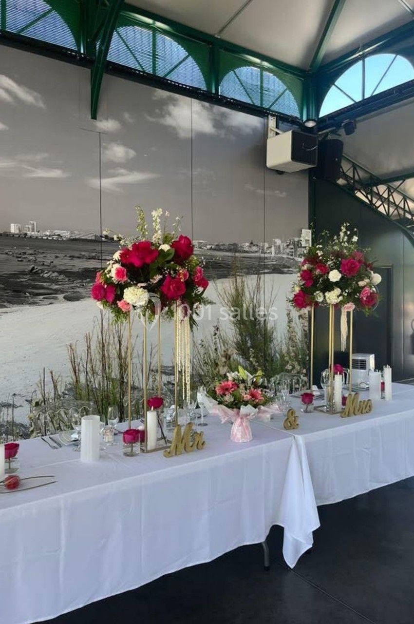Table décorée pour un mariage avec compositions florales roses et blanches, vue en arrière-plan d'un paysage côtier.