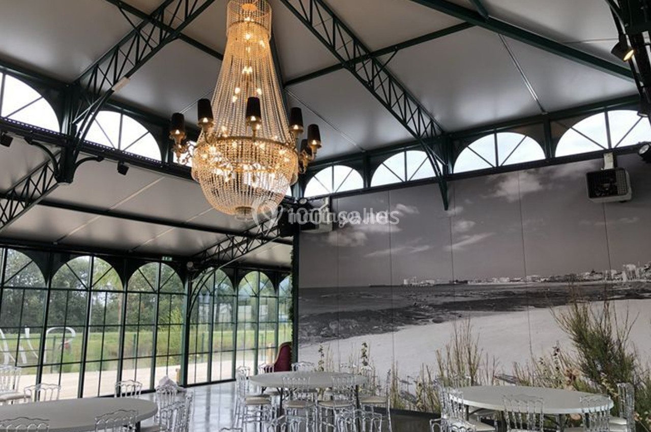 Salle lumineuse avec verrière, lustre imposant et tables rondes, décorée d'une grande photo en noir et blanc.