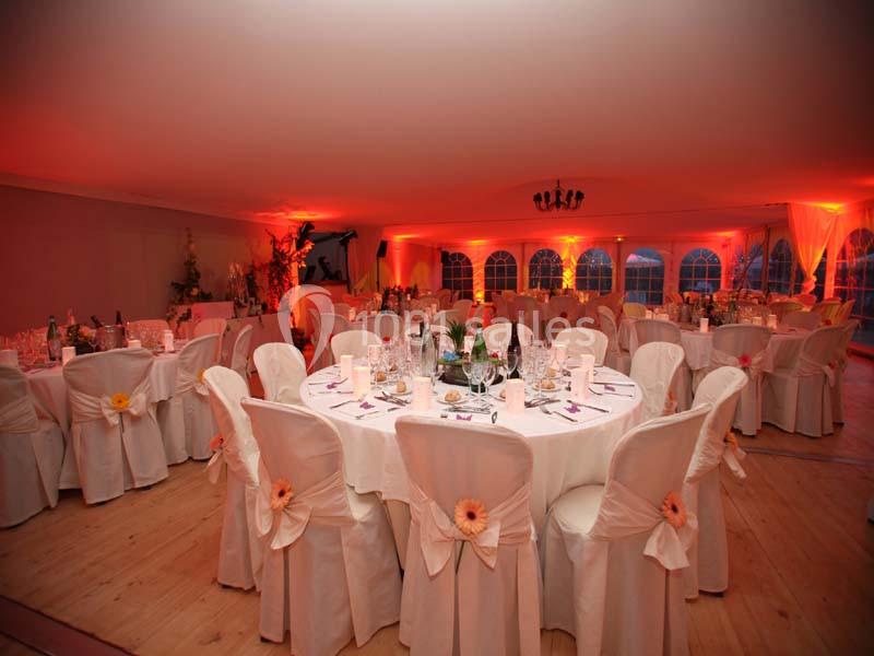 Salle de réception décorée avec des tables rondes, nappes blanches et chaises ornées de fleurs, éclairage tamisé.