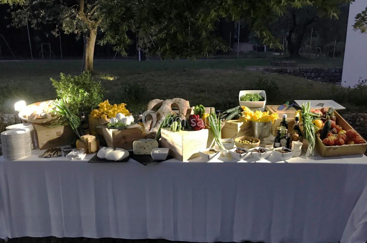 Table extérieure décorée avec des légumes frais, herbes, fromages et pains, éclairée dans un cadre verdoyant en soirée.