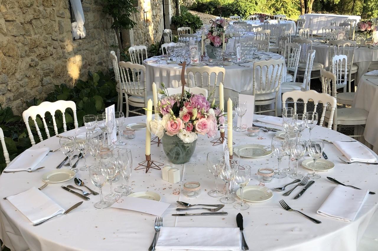 Table ronde élégamment dressée pour un événement, avec nappes blanches, bougies et centre de table floral.