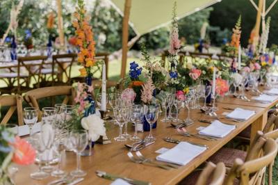 Miniature Traiteur Mouans-Sartoux (Alpes-Maritimes) - Jerome Ravel Traiteur #25 Table en bois décorée de fleurs colorées, verres, assiettes et couverts, installée en extérieur sous une tente.