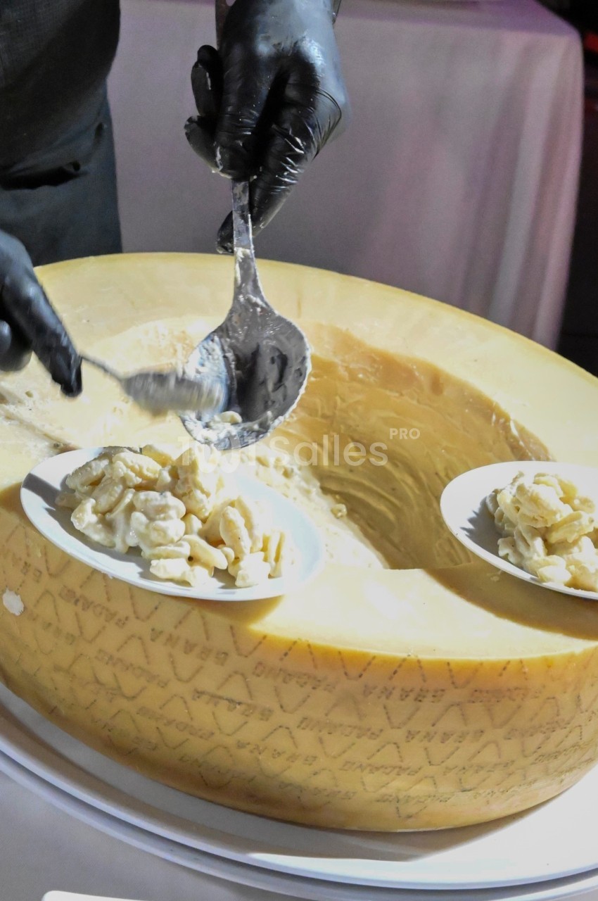 Un cuisinier sert des pâtes crémeuses directement dans une meule de fromage.