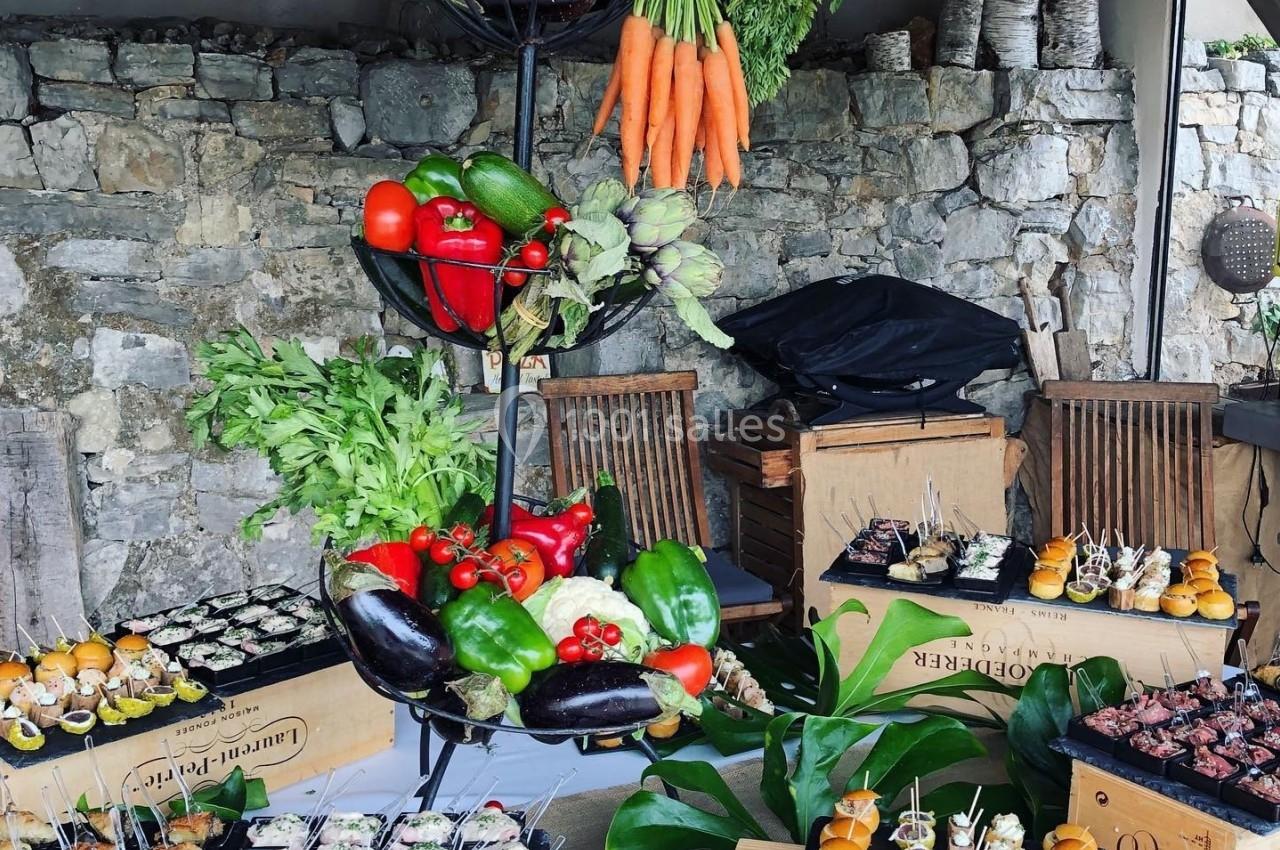Présentation de légumes frais et d'amuse-bouches variés sur une table en extérieur, décorée de manière rustique.