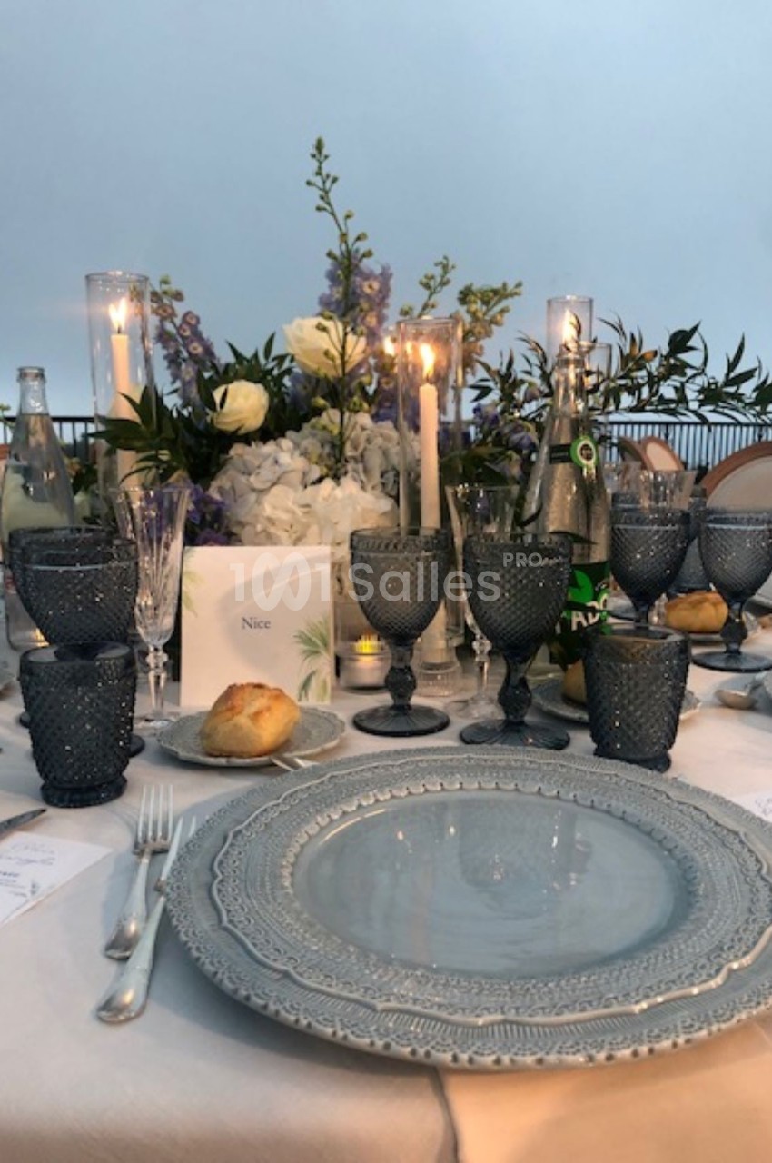 Table élégamment dressée avec vaisselle grise, verres en cristal, chandelles allumées et centre de table floral.