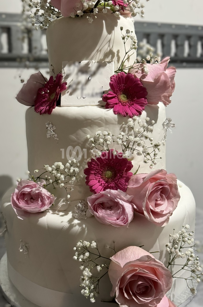 Gâteau de mariage à trois étages décoré de roses roses, de fleurs fuchsia et de gypsophile blanche.