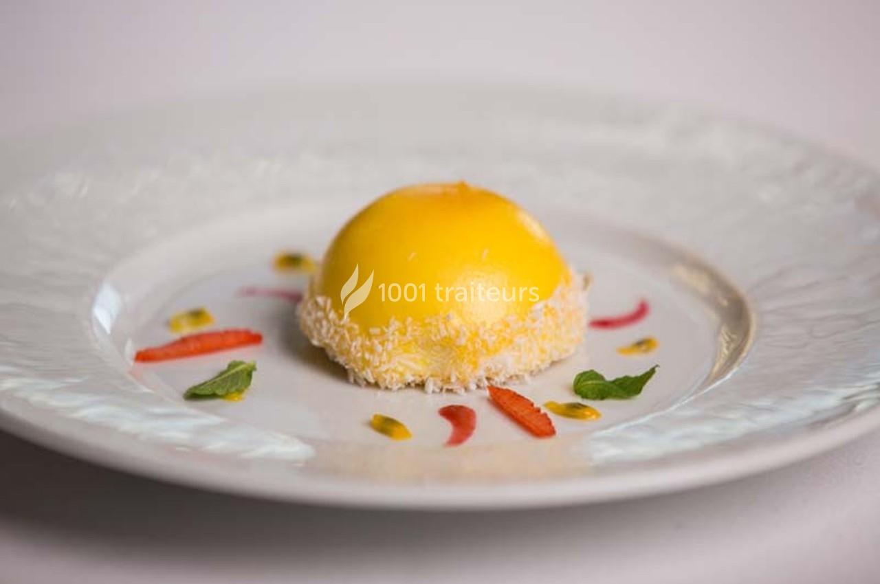 Dessert rond glacé jaune sur une assiette blanche, décoré de morceaux de fraise, menthe et coulis.