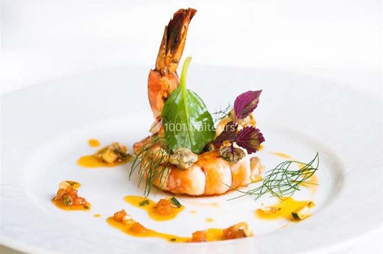 Crevette dressée sur une assiette avec sauce, herbes fraîches et feuilles décoratives.