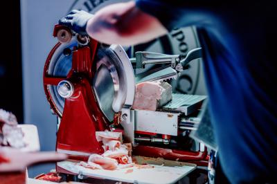 Personne utilisant une trancheuse rouge pour couper de la charcuterie dans un environnement professionnel.