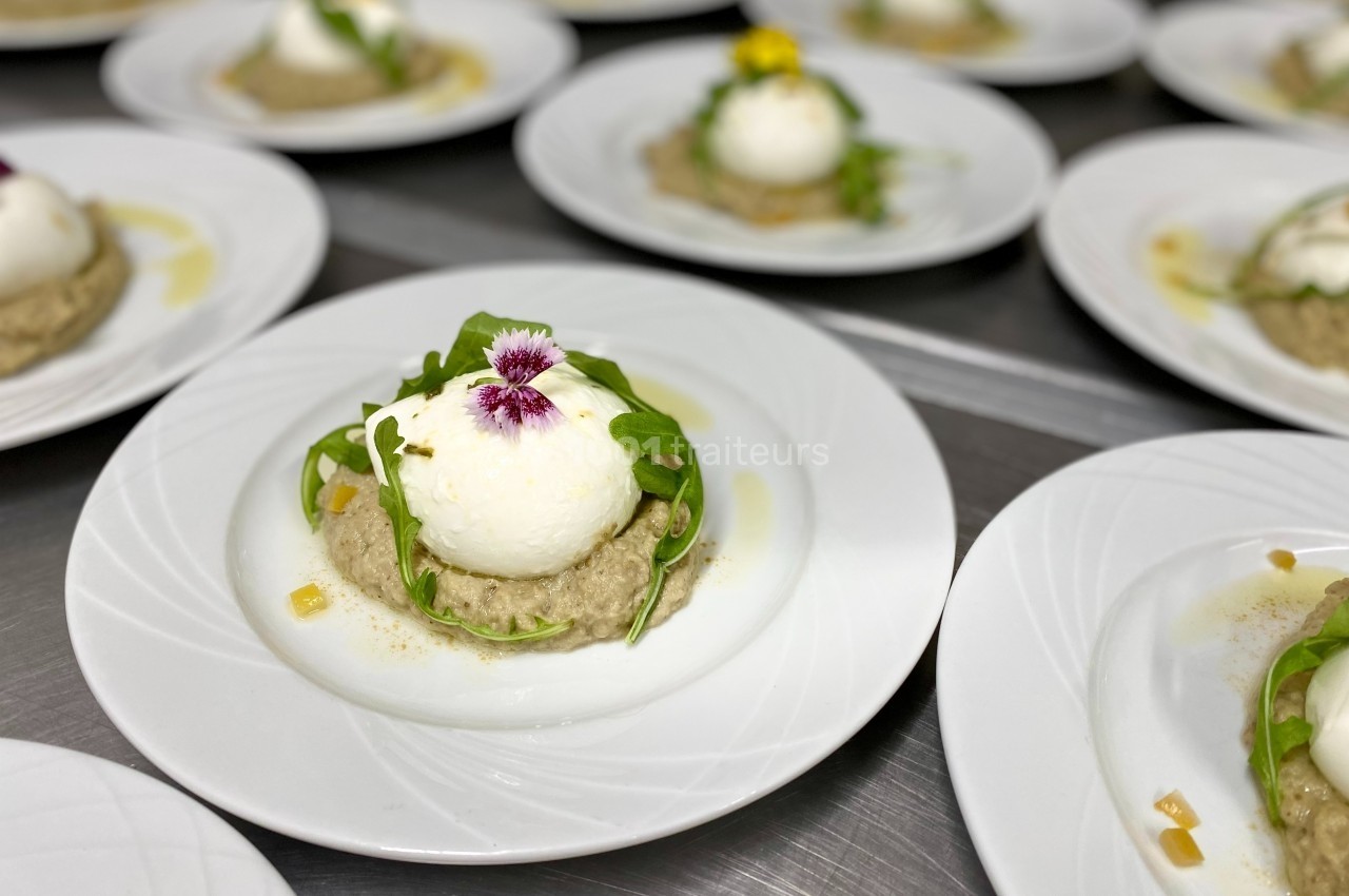 Assiettes de purée garnies de burrata, roquette et fleurs comestibles, disposées sur une table en inox.