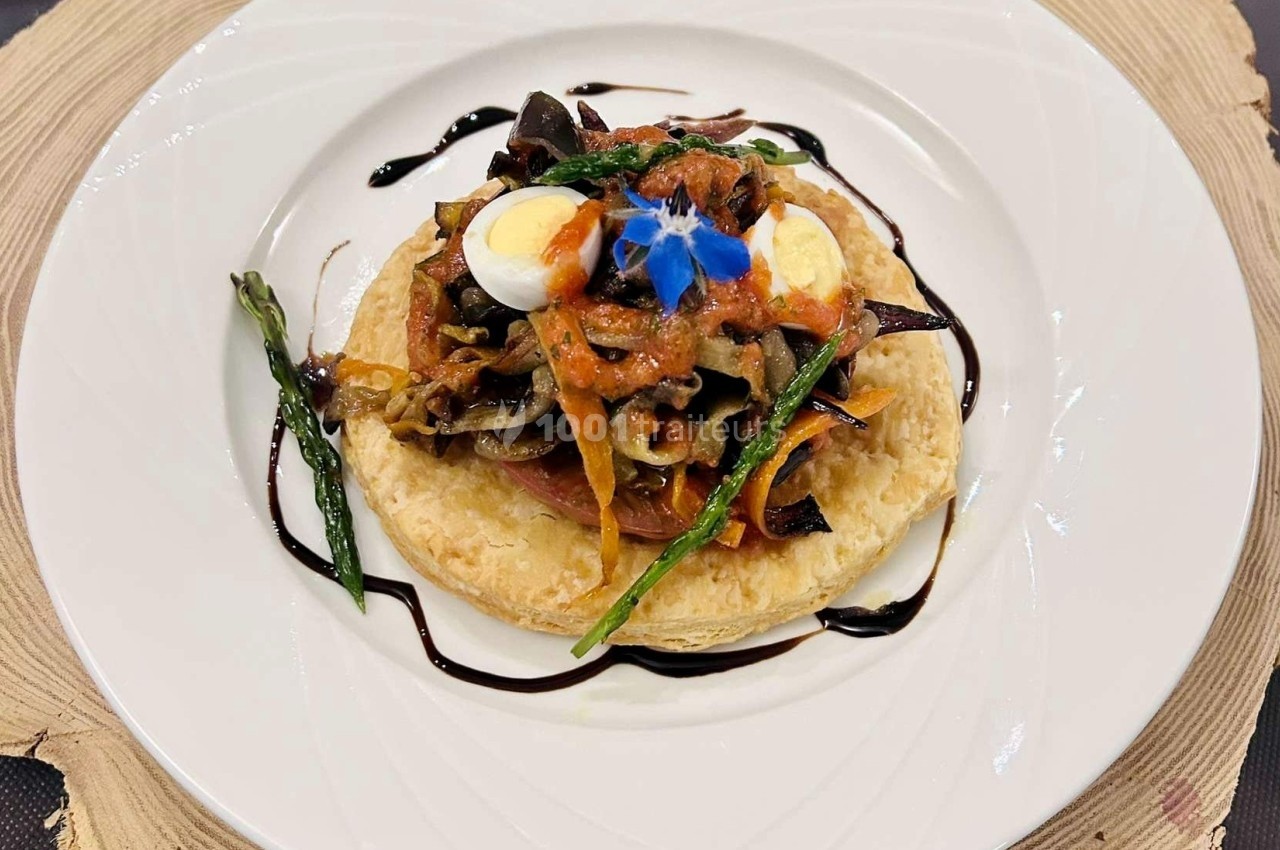 Tartelette garnie de légumes grillés, œufs de caille, asperges et sauce balsamique, servie sur une assiette blanche.