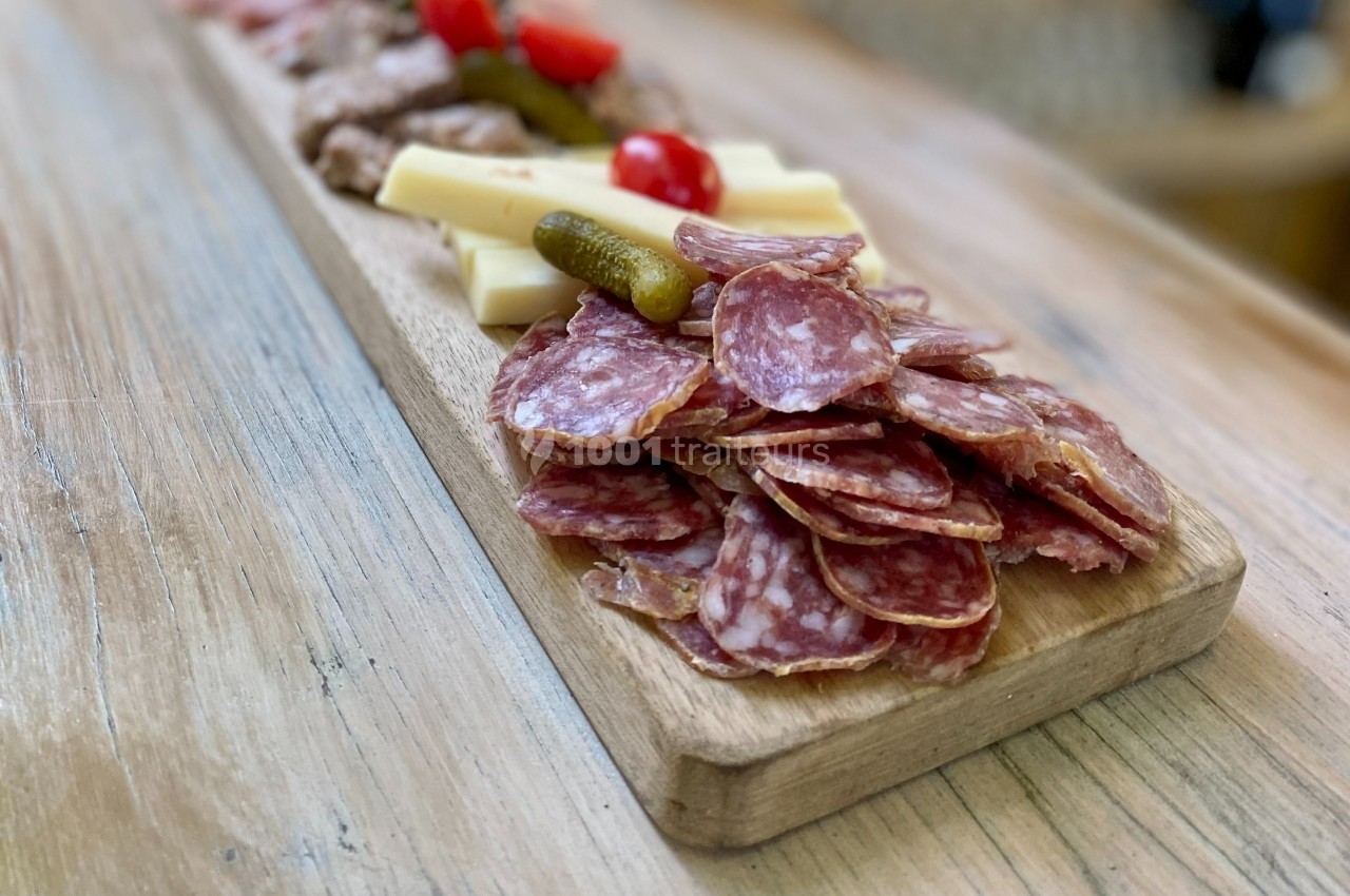 Planche en bois garnie de tranches de saucisson, fromages, cornichons et tomates cerises.