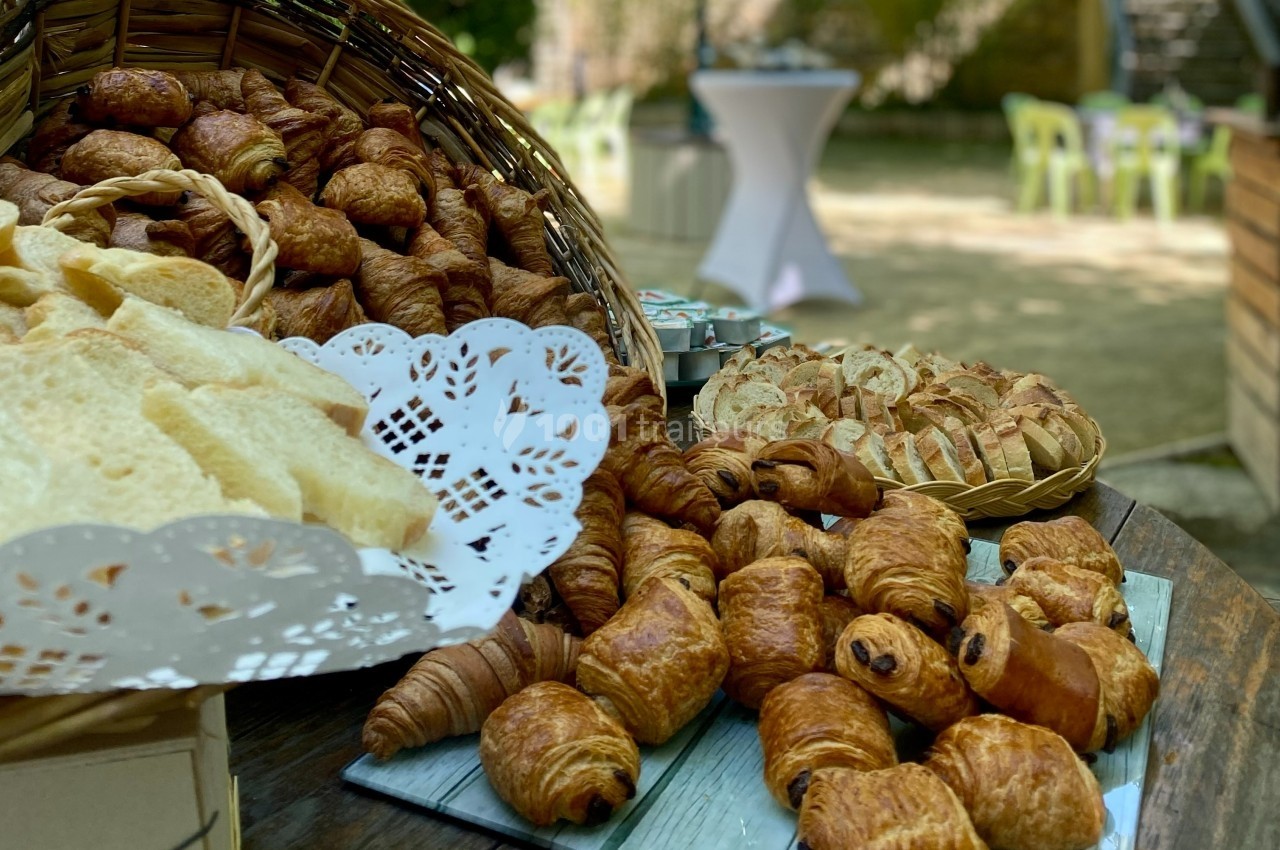 Assortiment de viennoiseries et de pains disposés sur une table en extérieur, avec un panier en osier en arrière-plan.