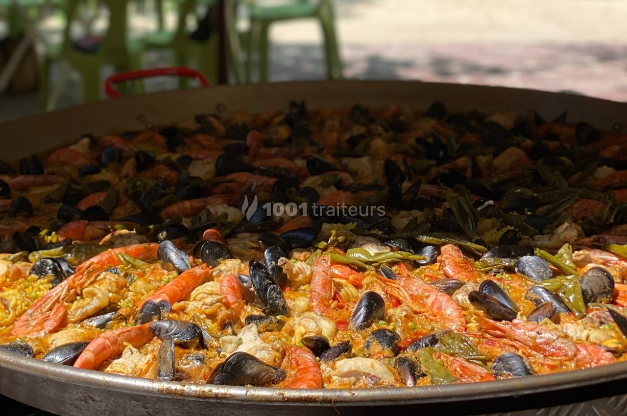 Grande poêle de paella garnie de fruits de mer, poulet, légumes et riz safrané, cuite en extérieur.