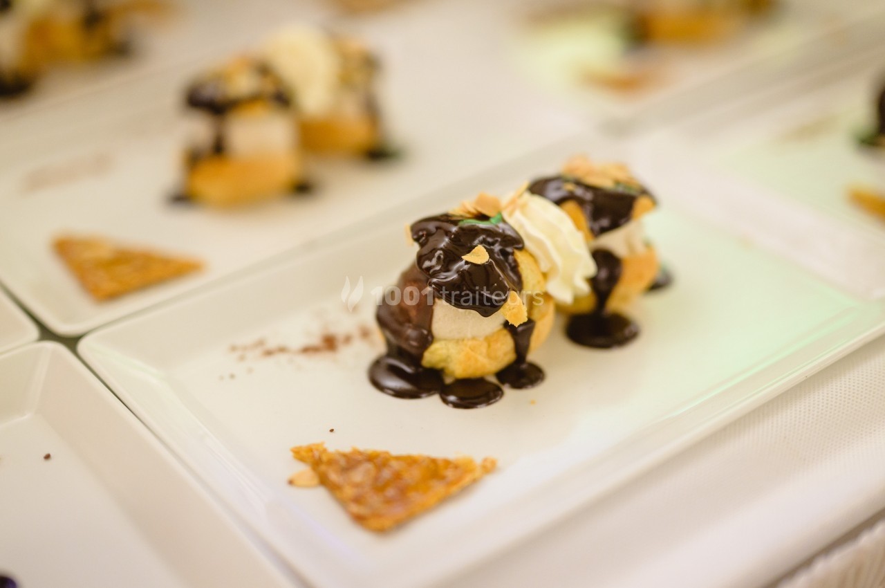 Assiette contenant des profiteroles nappées de chocolat, accompagnées d'un triangle de tuile croustillante.