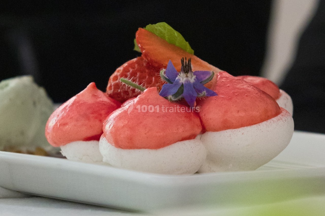 Meringue garnie de mousse rose, décorée de fraises fraîches, d'une fleur comestible et d'une feuille verte.