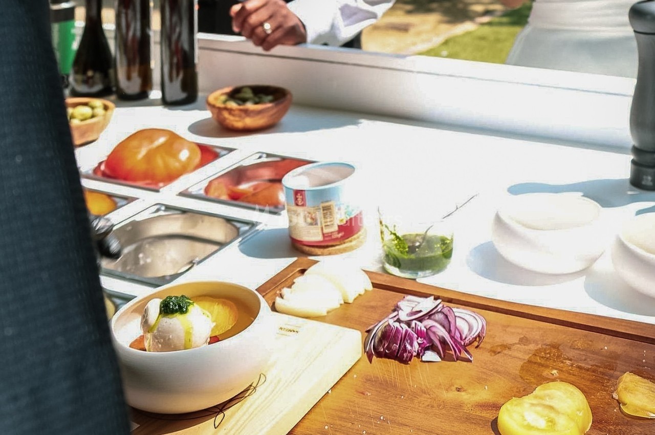 Préparation culinaire en extérieur avec des ingrédients frais, dont oignons rouges, fromage et condiments sur une table.