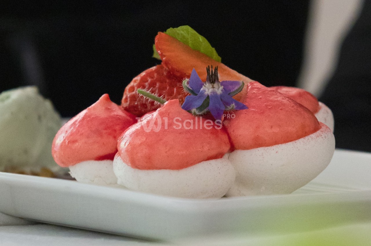 Meringue garnie de mousse rose, décorée de fraises fraîches, d'une fleur comestible et d'une feuille verte.