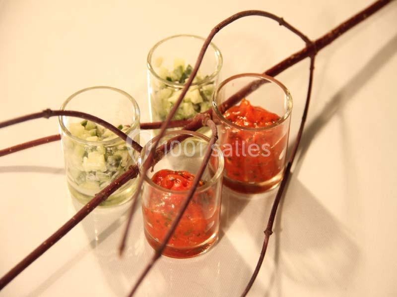Quatre verrines contenant des préparations rouges et vertes, décorées de branches fines sur une table blanche.
