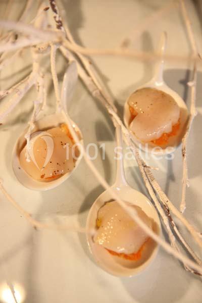 Trois cuillères blanches contenant des noix de Saint-Jacques sur une purée orange, décorées de branches blanches.