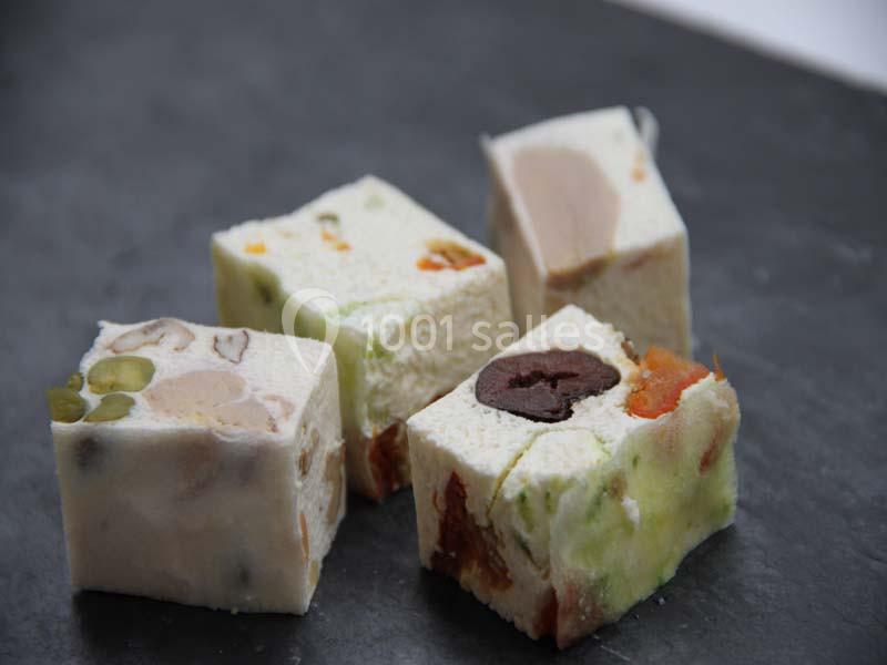 Quatre morceaux de nougat aux fruits secs et confits, posés sur une surface sombre.