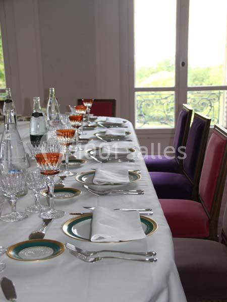 Table dressée avec vaisselle élégante, verres et serviettes blanches, devant une fenêtre lumineuse avec vue sur un balcon.
