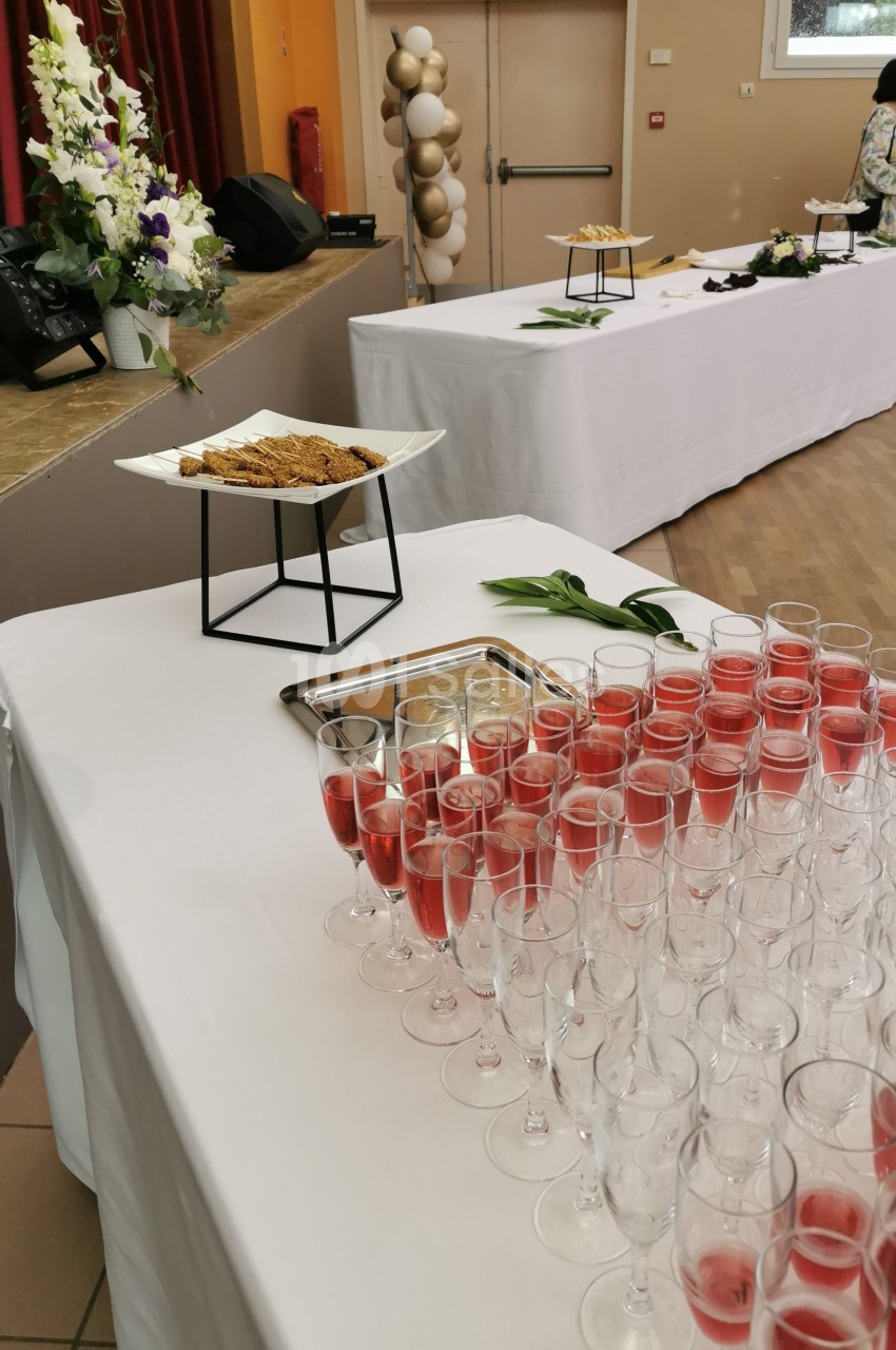 Table dressée avec des flûtes de cocktail rouge, des biscuits apéritifs et des décorations florales en arrière-plan.