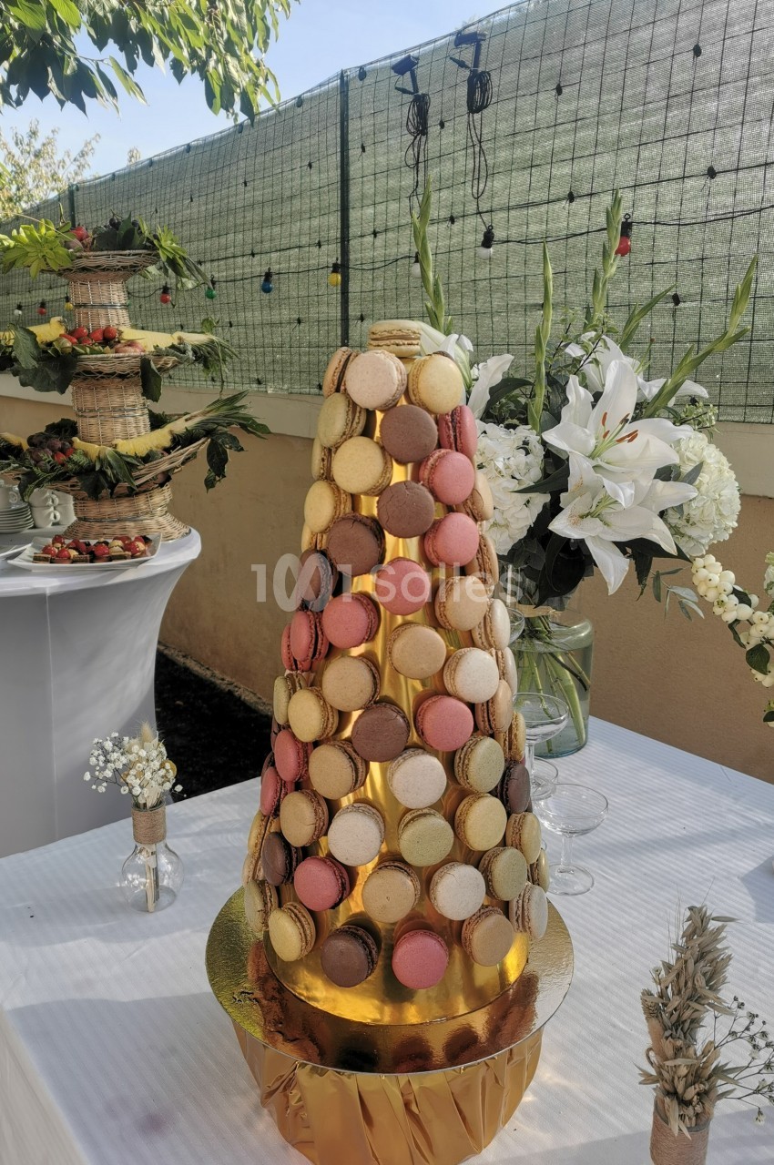 Tour de macarons colorés sur une table blanche, entourée de décorations florales et d'autres desserts en extérieur.