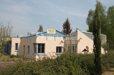 Table dressée avec nappes blanches, couverts, menus et bouquets de fleurs, entourée de chaises en bois dans une salle.