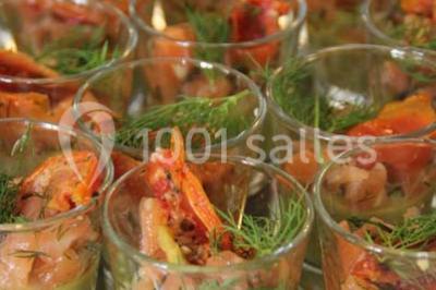 Table dressée avec nappes blanches, couverts, menus et bouquets de fleurs, entourée de chaises en bois dans une salle.