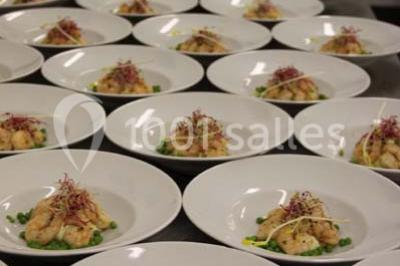 Table dressée avec nappes blanches, couverts, menus et bouquets de fleurs, entourée de chaises en bois dans une salle.