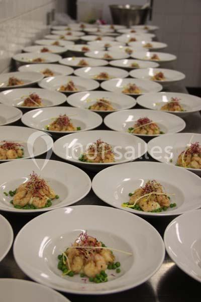 Assiettes alignées contenant des plats de crevettes, petits pois et germes, disposées dans une cuisine professionnelle.