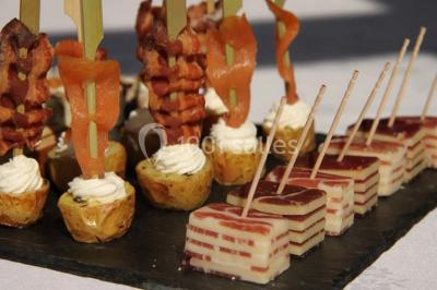 Table dressée avec nappes blanches, couverts, menus et bouquets de fleurs, entourée de chaises en bois dans une salle.