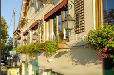 Table dressée avec nappes blanches, couverts, menus et bouquets de fleurs, entourée de chaises en bois dans une salle.