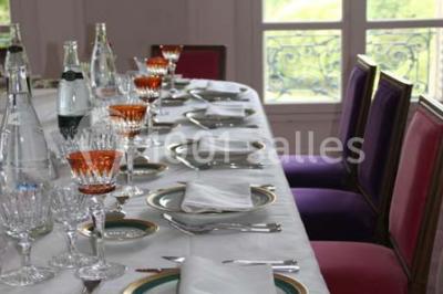 Table dressée avec nappes blanches, couverts, menus et bouquets de fleurs, entourée de chaises en bois dans une salle.