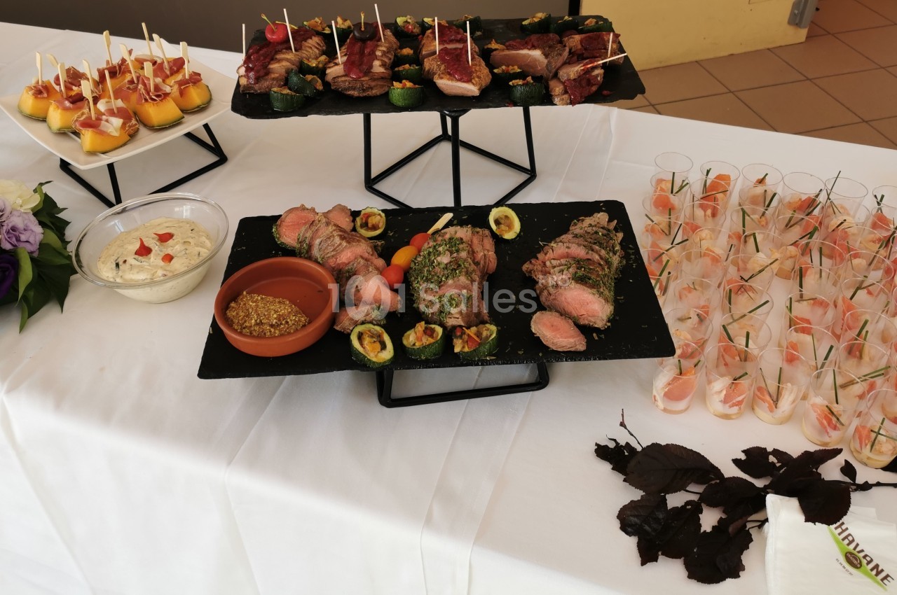 Plateau de buffet avec viandes grillées, verrines, dips, brochettes apéritives et décoration florale sur nappe blanche.