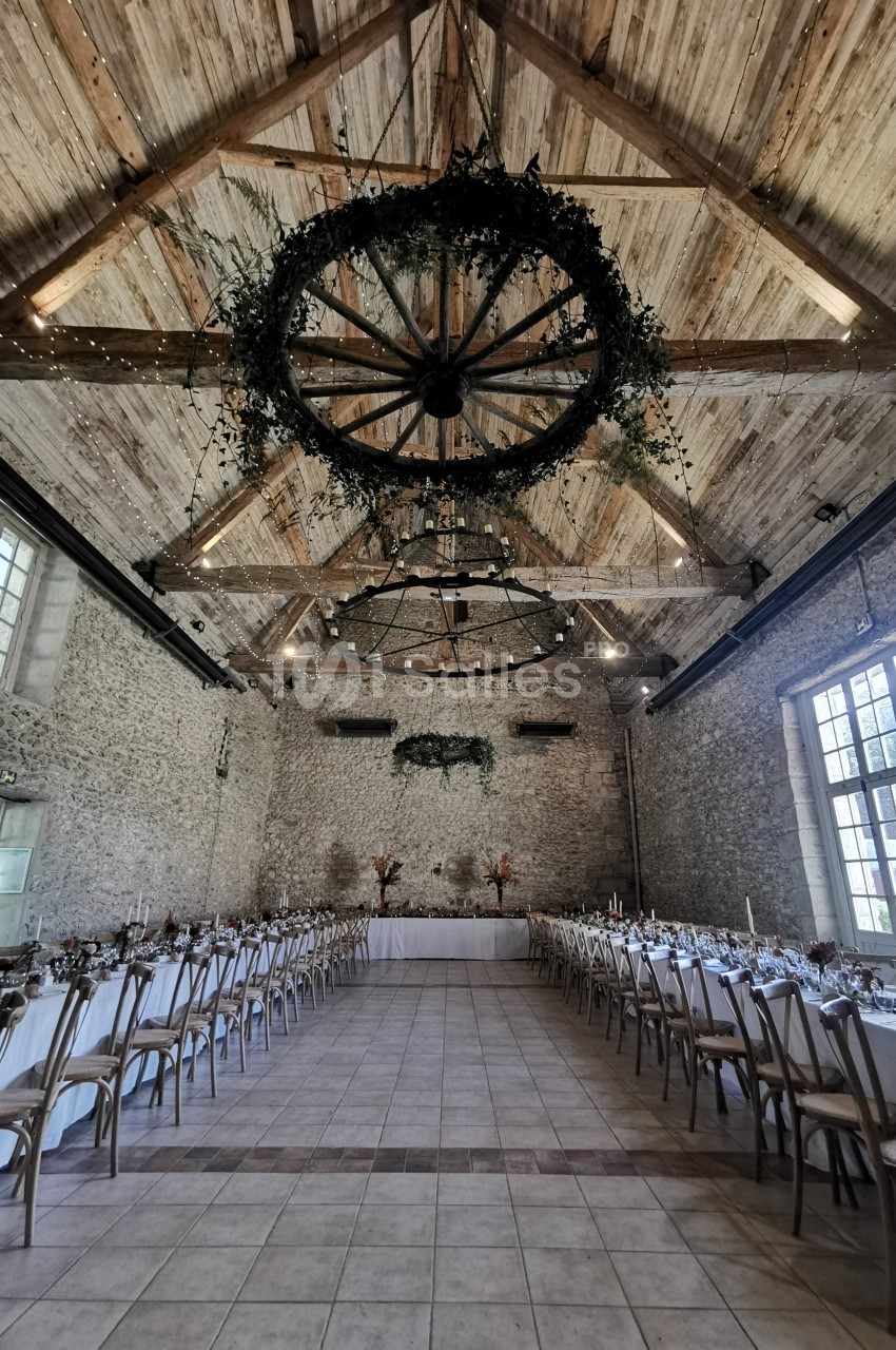 Salle de réception en pierre avec plafond en bois, tables décorées et suspensions végétales circulaires.