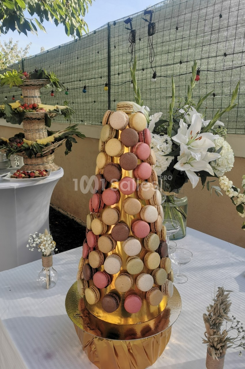 Tour de macarons colorés sur une table blanche, entourée de décorations florales et d'autres desserts en extérieur.