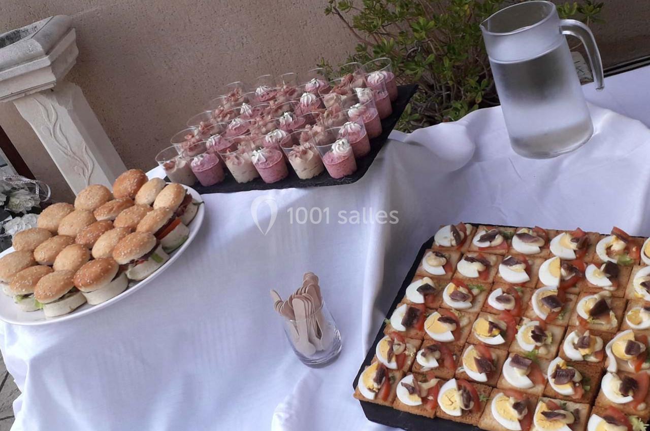 Plateau de mini-burgers, verrines sucrées et toasts garnis, disposés sur une table avec une carafe d'eau.