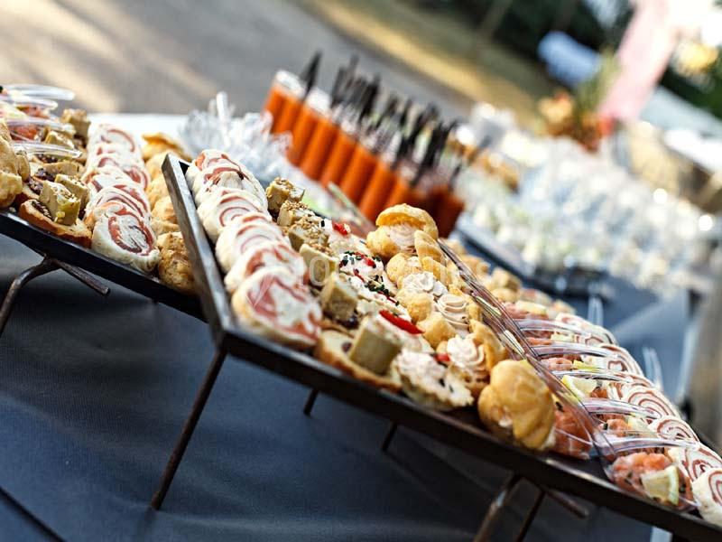 Plateaux de bouchées salées et sucrées disposés sur une table lors d'un événement en extérieur.