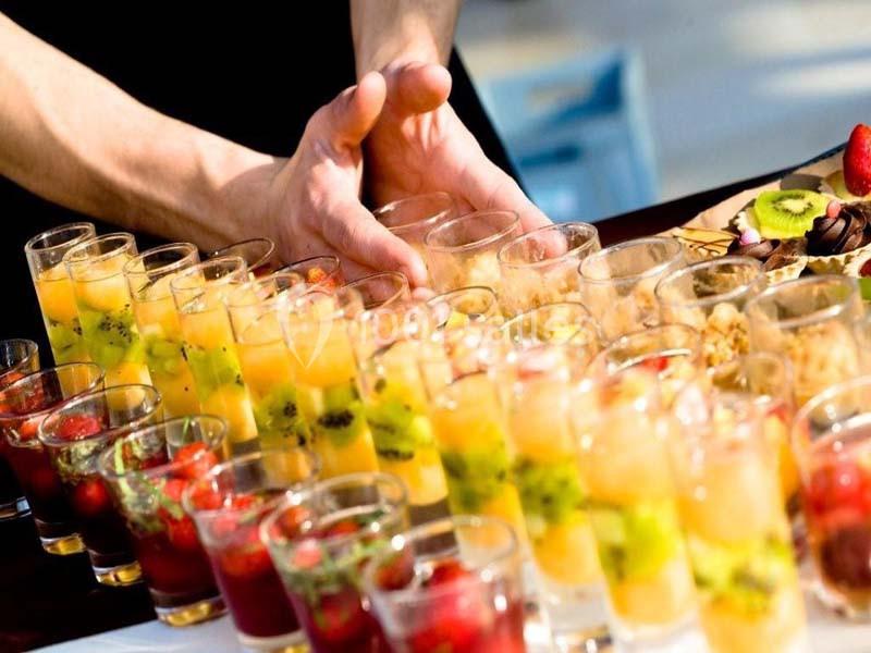 Alignement de verrines colorées contenant des fruits frais, avec des mains disposant les verres sur une table.