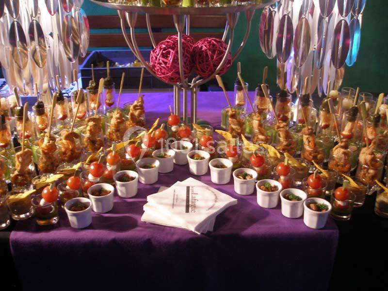 Buffet coloré avec brochettes, verrines et décorations sur une nappe violette.